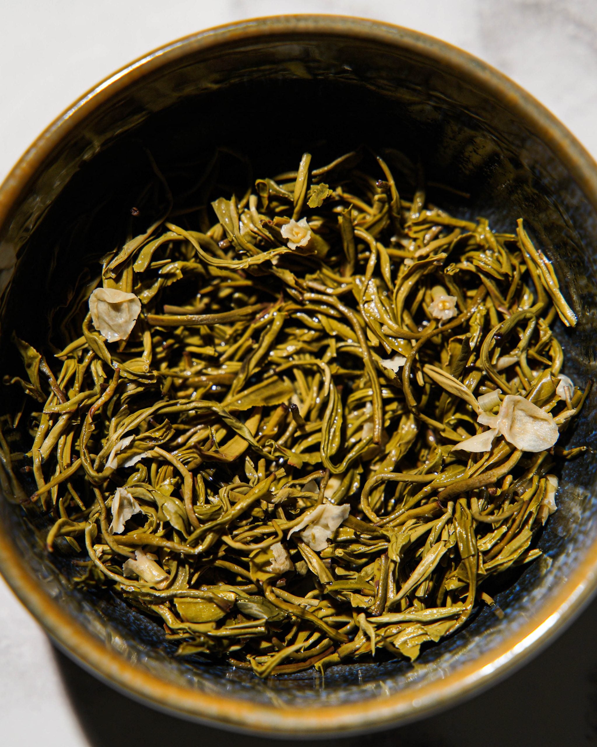 Close-up of Chinese jasmine green tea wet leaves in a dark ceramic bowl