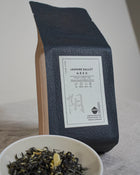 Tea packaging with a YIN CHA tea label and a bowl of Chinese jasmine green tea leaves on a neutral background